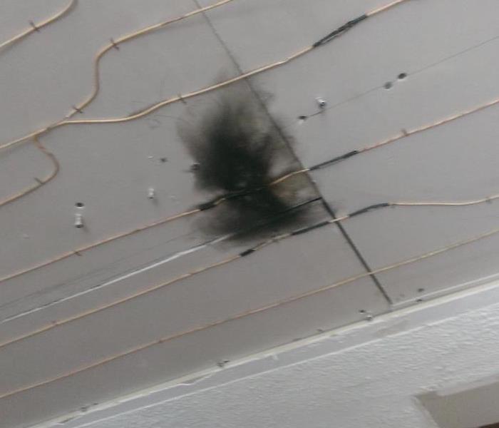small black burnt hole damage in white ceiling